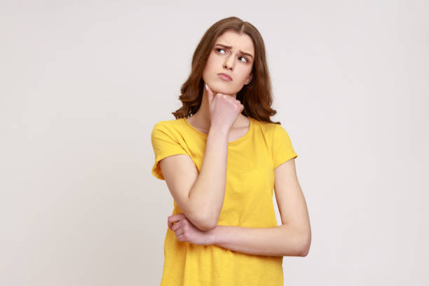 портрет привлекательной девушки-подростка с каштановыми волнистыми волосами в желтой футболке, думающей о важных вещах, держащей подбород - pensive question mark teenager adversity стоковы�е фото и изображения