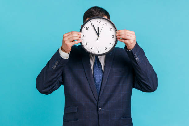 istock Unknown male person wearing official style suit hiding face behind wall clock display, wasting his time, procrastination, organization of working time. 1343293511