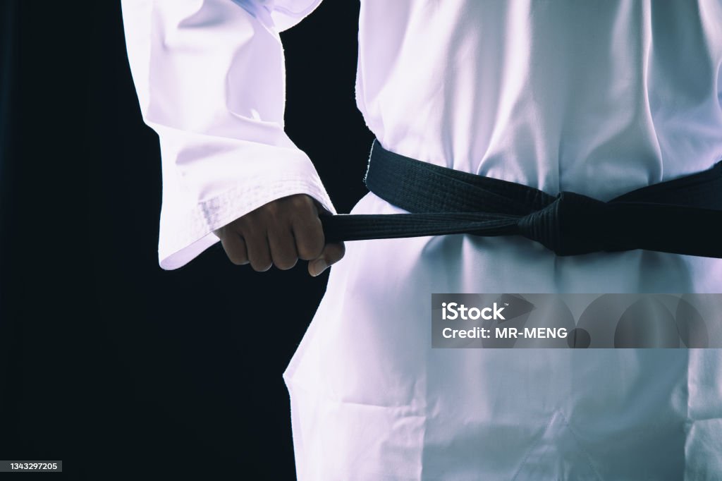 Close up Taekwondo martial arts fighter in white uniform holding black belt Close up Taekwondo martial arts fighter in white uniform holding black belt on dark background Black Belt Stock Photo