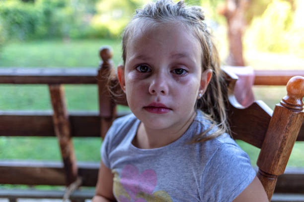 Sad crying Caucasian little girl. Close up portrait of crying beautiful little girl with outdoors background. A embarrassed unhappy little kid sitting alone shy and crying.