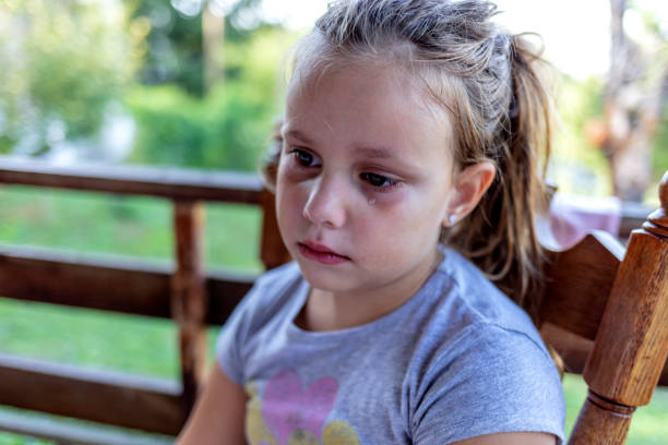 Sad crying Caucasian little girl. Close up portrait of crying beautiful little girl with outdoors background. A embarrassed unhappy little kid sitting alone shy and crying.
