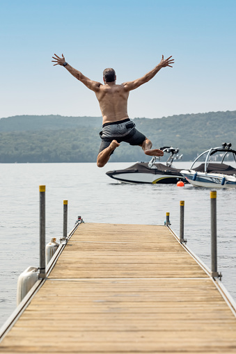 Man jumping with his arms in the air off the end of a jetty, pier at a lake in summer. Lac Saint-Joseph, Fossambault-sur-le-lac, Quebec, Canada