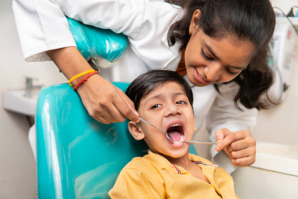 heureuse assistante dentiste examinant les dents de petits garçons à la clinique. - dentist teenager dental hygiene sitting photos et images de collection