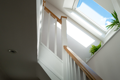 Abstract view of a newly installed loft conversion seen from the ground floor, looking at the staircase. A skylight window is seen on a sunny day.