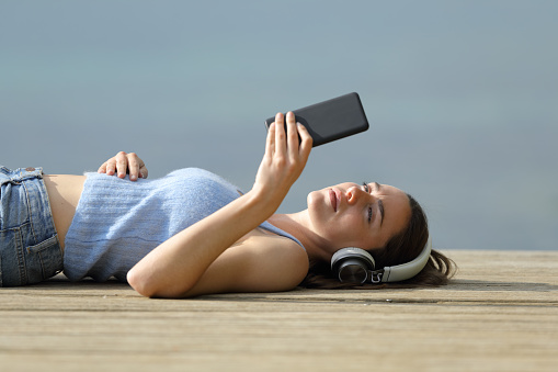Woman lying on pier listening to music with phone