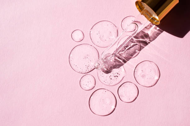 ピンクの背景にヒアルロン酸とガラスピペットの透明な滴。上のビュー、テキストの場所。 - ヒアルロン酸 ストックフォトと画像