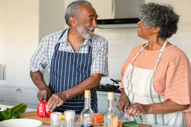 feliz pareja de ancianos americanos arfican cortando verduras y preparando la comida juntos - cooking senior adult healthy lifestyle couple fotografías e imágenes de stock