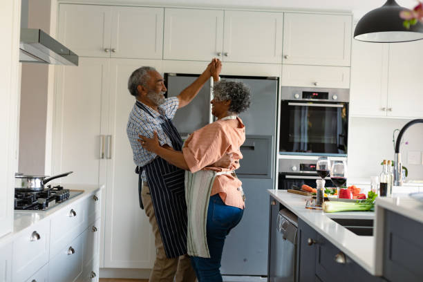 Happy arfican american senior couple dancing together in kitchen and having fun stock photo