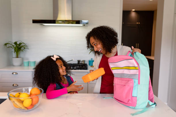 счастливые афроамериканки мать и дочь готовят ланч-бокс для школы - lunch box child education school стоковые фото и изображения