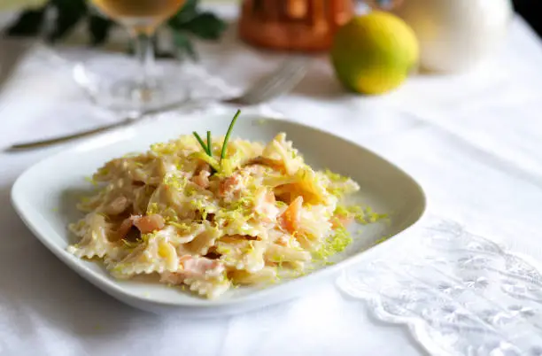 Farfalle pasta with smoked salmon, a cream sauce and lemon on white plate. Italian food.
