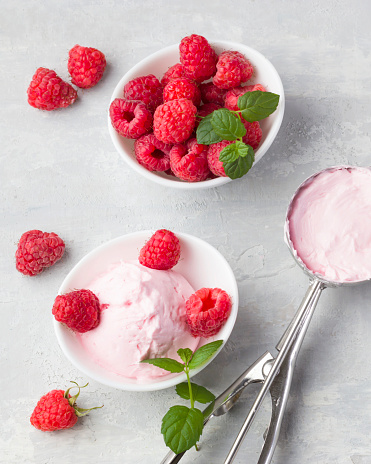 Fresh raspberries with mint and homemade ice cream in a white cup on a light background. Stainless steel spoon for ice cream balls. Delicious and romantic dessert. Top view. Copy space.