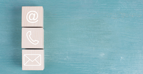 Symbols for e-mail, phone and newsletter on wooden blocks, blue background