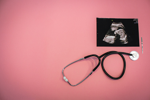 Stethoscope, ultrasound image of a baby and a pregnancy test on a pink background. Flat-lay, top view with place for your text. Medical trends and concept.