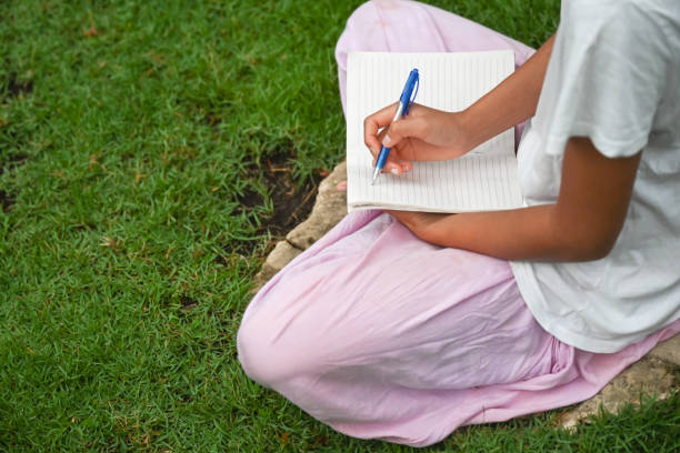 Beautiful girl writting in a notebook sitting in the grass