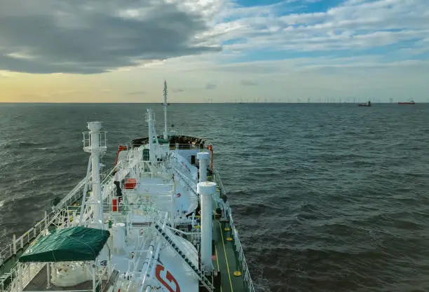 Gas-carrier sailing close to coastline with wind power plant and cloudy sky background