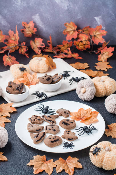 istock Ready-to-eat halloween treat - gingerbread cookie with chocolate icing on a plate on the table with pumpkins and leaves. Traditional celebration. Vertical view 1343349299