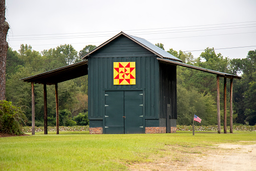 Lenox, Georgia - September 17, 2021: A painted wooden pole barn on a rural Georgia cotton farm displays a traditional windmill quilt pattern in red and yellow. A cotton field is visible in the background.