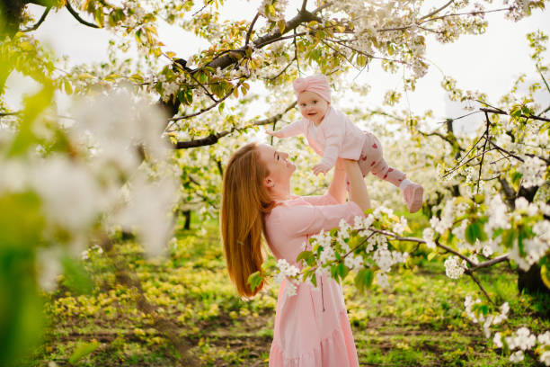 mother with baby in arms in flowering garden. surgery for child with cleft lip. mother with baby daughter in her arms in the flowering spring garden. surgery for a child with a cleft lip. Children's surgery and medicine. walks with children. happy childhood. beauty and love. cleft lip stock pictures, royalty-free photos & images