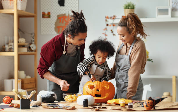 felice famiglia afroamericana madre, padre e figlio che intagliano la zucca per le vacanze di halloween insieme a casa - halloween pumpkin party carving foto e immagini stock