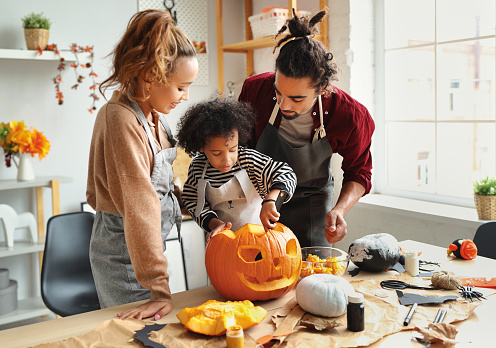 Feliz familia afroamericana madre, padre e hijo tallando calabaza para las vacaciones de Halloween juntos en casa photo