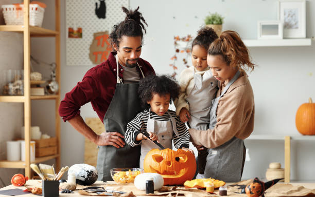 grandes padres de familia afroamericanos felices con dos niños preparándose para la celebración de halloween - orange halloween fotos fotografías e imágenes de stock