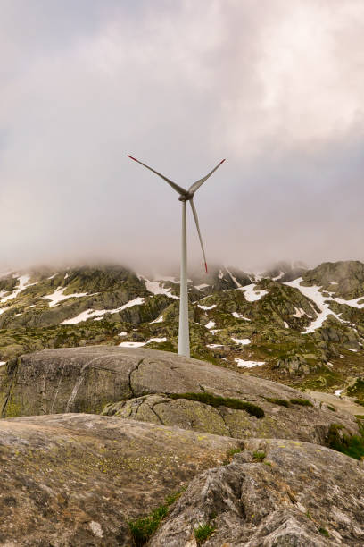 Wind turbine frontside surrounded by partially snow covered rocks on the top of the gotthard pass in switzerland on a cloudy and foggy summer day