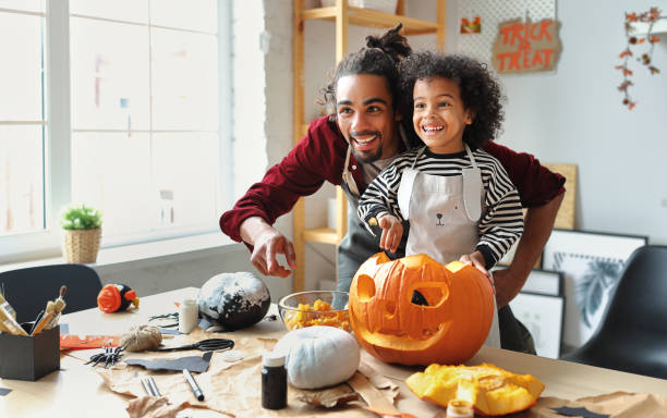 padre étnico quitando pulpa de calabaza madura mientras talla jack o linterna con hijo pequeño para halloween - halloween pumpkin party carving fotografías e imágenes de stock