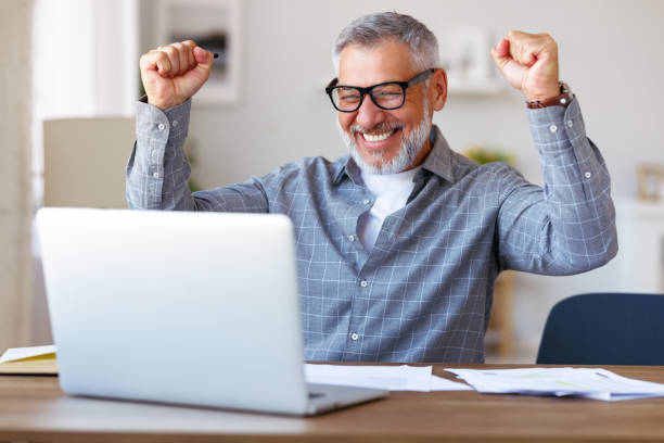 homme âgé excité célébrant le succès, obtenant de bons résultats aux examens pendant l’éducation à distance - good news photos et images de collection