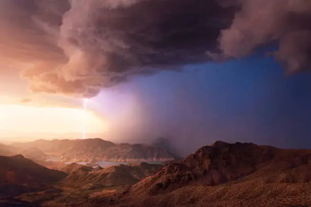 A powerful monsoon thunderstorm with lightning and heavy rain drifts over Lake Mead at sunset.