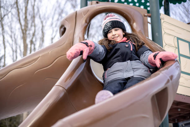 garotinha deslizando um escorregador no playground ao ar livre no inverno - playground snow winter little girls - fotografias e filmes do acervo