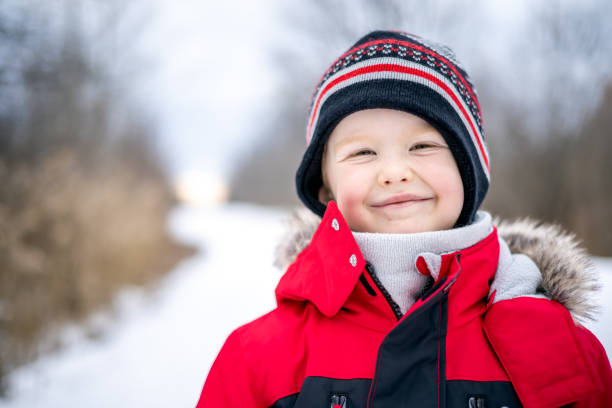 Little Boy Sliding Down a Slide at the Playground Outdoors in Winter. He is very happy and smiling. It is a cold winter day and he is wearing warm clothing.