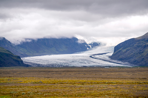 One of Vatnajokull glaciers tongues at Skaftafell National park in Iceland from the circular road. Upper part of photo is covered by clouds and front part by green grass.