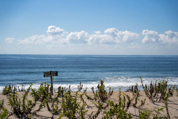 Keep off dunes sign at Rockaway Beach, Queens, New York City. Sunny Day with clouds and waves.