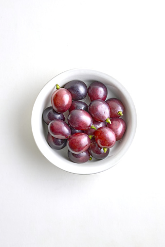 Fresh purple grapes in a white porcelain bowl on a white background