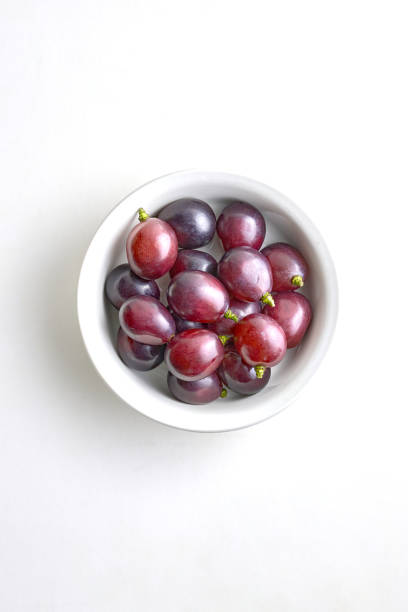 uvas roxas frescas em uma tigela de porcelana branca em um fundo branco - red grape grape fruit sweet food - fotografias e filmes do acervo