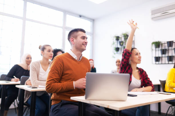 istock Multi ethnic students listening to a lecturer in a classroom. Smart young people rasing hands during class. 1343407850