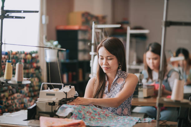 trabajadora asiática china de cuello azul que trabaja en un estudio de costura en una fila - chinese production fotografías e imágenes de stock