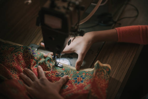 close up top view high angle asian chinese teenage girl's hand holding batik sewing stitching on sewing machine illuminated by led light - seam needle textile industry thread fotografías e imágenes de stock