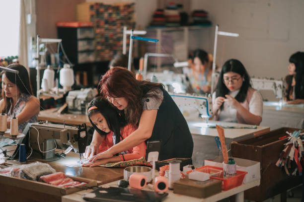 donna asiatica cinese matura sarto che insegna al suo studente di cucito l'abilità di cucito con la macchina da cucire nel suo studio - sewing women tailor teenage girls foto e immagini stock