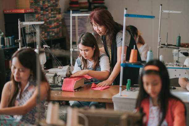 donna asiatica cinese matura sarto che insegna al suo studente di cucito l'abilità di cucito con la macchina da cucire nel suo studio - sewing tailor sewing machine women foto e immagini stock