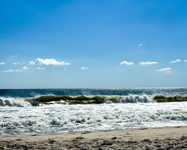 istock Waves crashing on beach, with blue sky above 1343427442