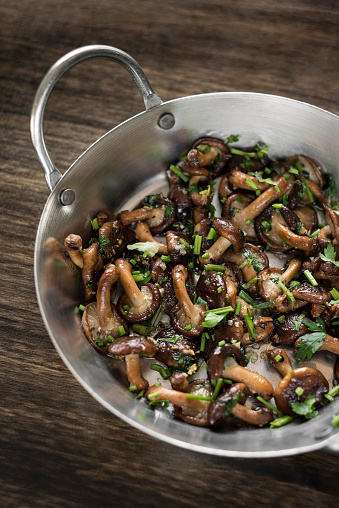 fried Shiitake mushrooms sauteed with garlic and herbs in metal pan on wood table