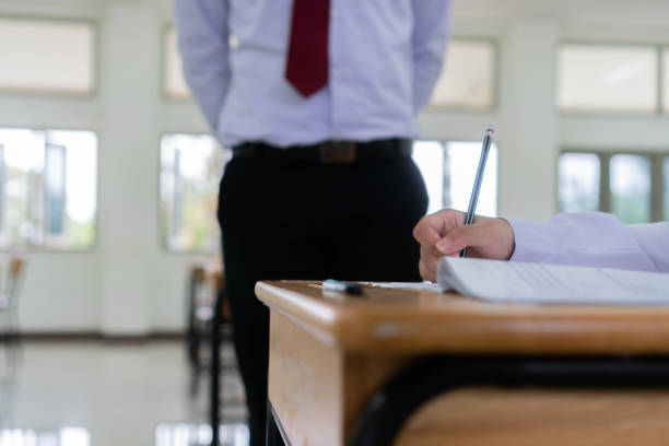 ritorno a scuola, insegnante asiatico intelligente che supervisiona l'esame in sala esami cercando tutti gli studenti del liceo in sala prove mentre gli studenti tailandesi uniformi concentrano l'ammissione nelle scuole secondarie thailandia - emotional stress looking group of people clothing foto e immagini stock