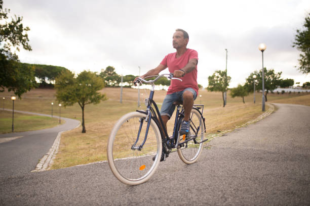 homem confiante e maduro andando de bicicleta ao longo da estrada do parque - cycling shorts - fotografias e filmes do acervo