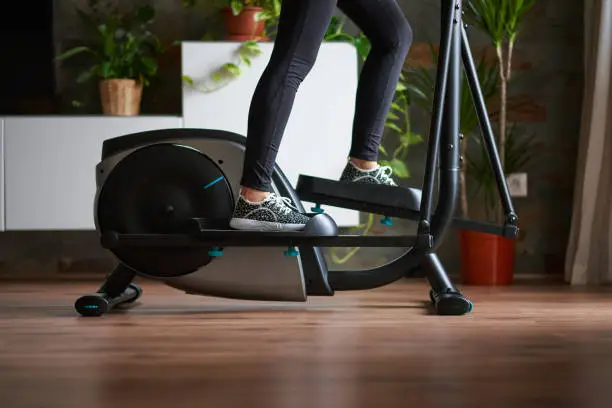 Woman legs training on smart elliptical trainer indoors at home in daylight with natural light