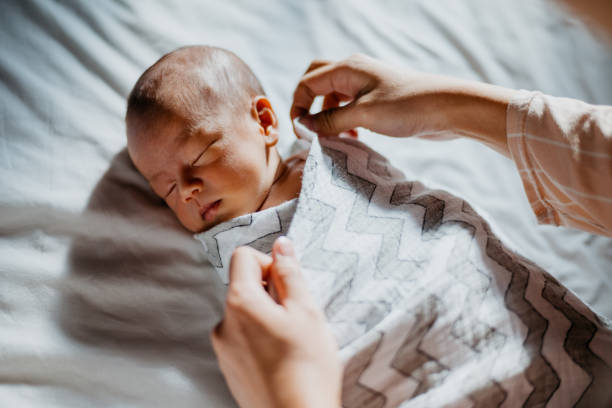 mutter wickelt ihr neugeborenes baby aufs bett - einwickeln stock-fotos und bilder