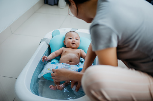 Image of an Asian Chinese woman taking a bath for her baby. Mother cleaning her baby boy with cloth and warm water in baby bathtub.