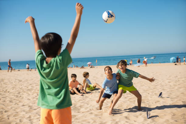 Boys fighting for ball when playing football. Excited preteen friends playing soccer on beach. Youth sport, summer vacation concept