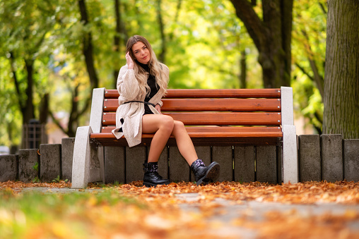 Pretty face girl sitting lonely on bench in autumn park.