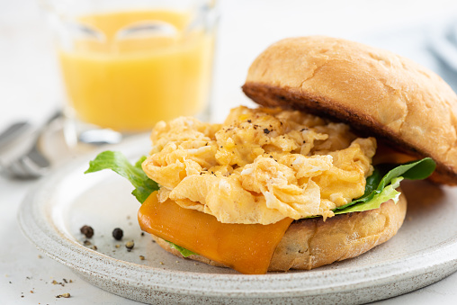 English muffin with scrambled eggs and cheese for breakfast served with glass of orange juice